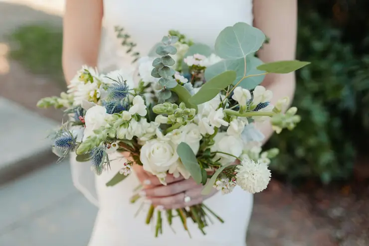 A bride holding a loose bouquet of white flowers, eucalyptus and thistle