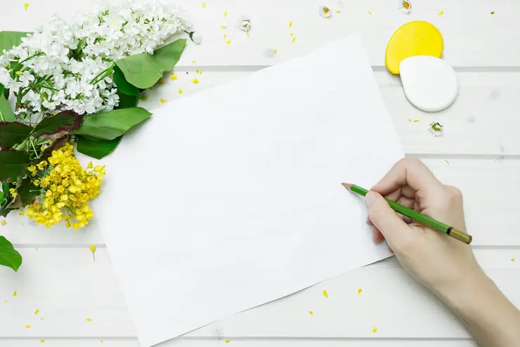 A hand writing a card on a white table beside a bunch of flowers