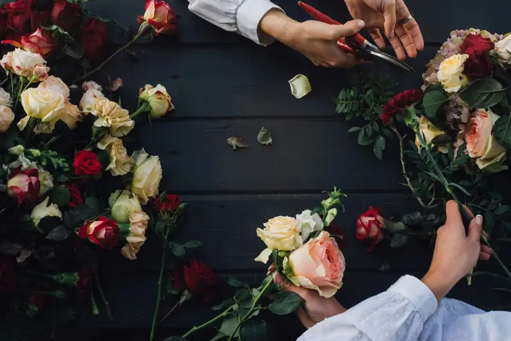 A florist's hands building a bouquet of roses on a dark work table