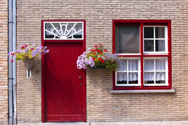A red front door with flower boxes on the windowsills